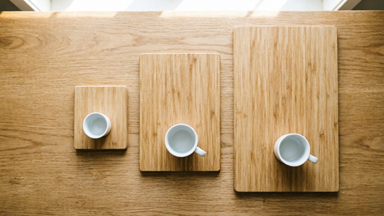 Three rectangular bamboo tea trays of increasing sizes arranged in a row from smallest to largest, each holding a small gaiwan and cup for scale